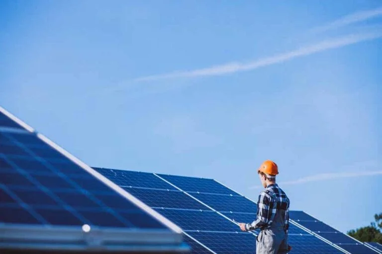 Technician in an orange hard hat inspecting rows of solar panels